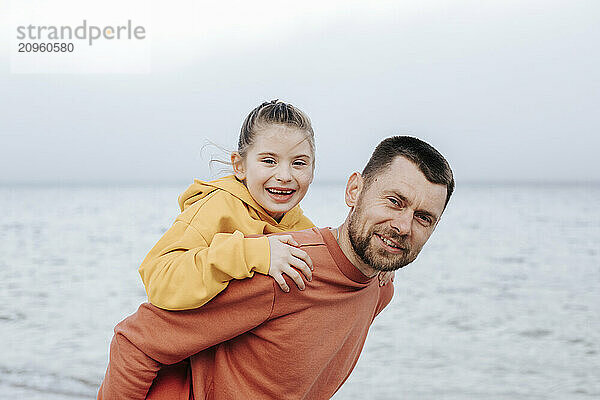 Smiling father giving piggy back ride to daughter at beach