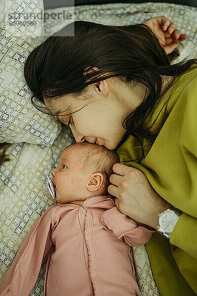 Mother kissing newborn baby girl lying on bed