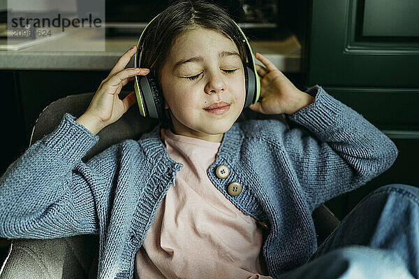 Girl with eyes closed listening to music through wireless headphones at home