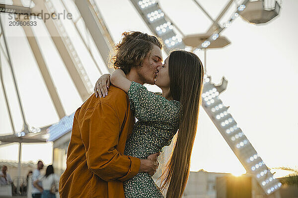 Girlfriend and boyfriend kissing at sunset in amusement park