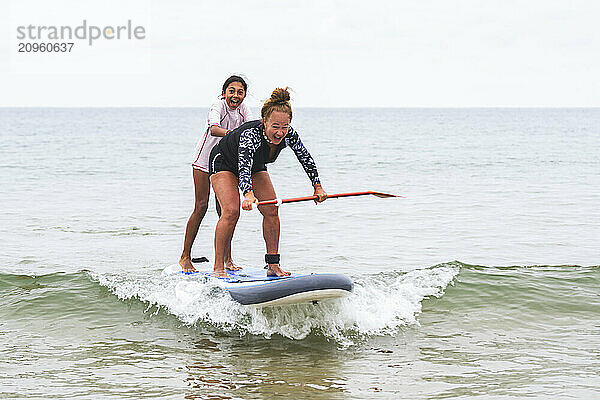 Grandmother and granddaughter surfing on paddle board at sea