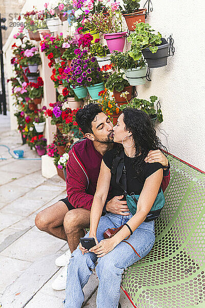 Romantic couple kissing each other sitting on bench near plants