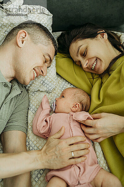 Smiling parents lying on bed with newborn baby