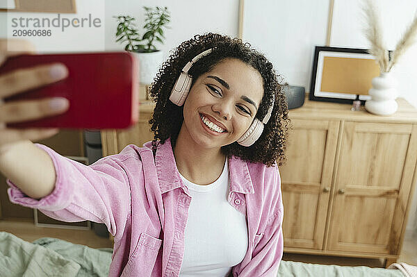 Happy teenager wearing wireless headphones clicking selfie through smart phone