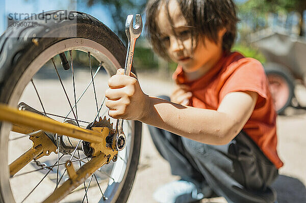 Boy repairing old bicycle using wrench in back yard