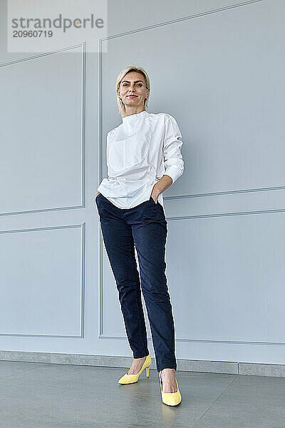 Smiling businesswoman with hands in pockets standing in front of wall