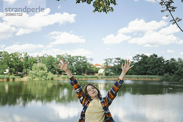 Carefree boy with arms raised in plaid shirt near lake