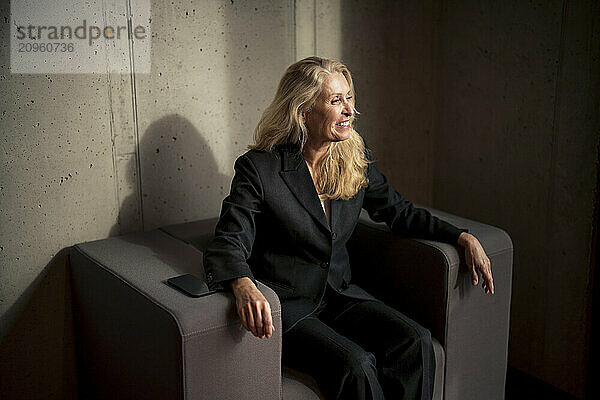 Happy senior businessman with blond hair sitting on armchair at office