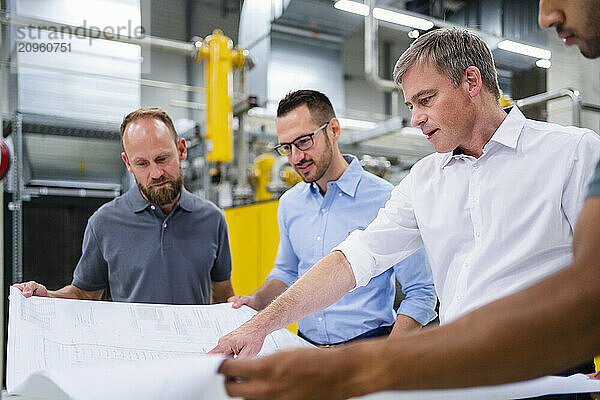 Businessmen and employees having a meeting in factory looking at plan