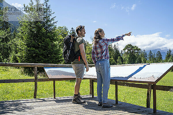 Hikers standing and pointing near maps at sunny day