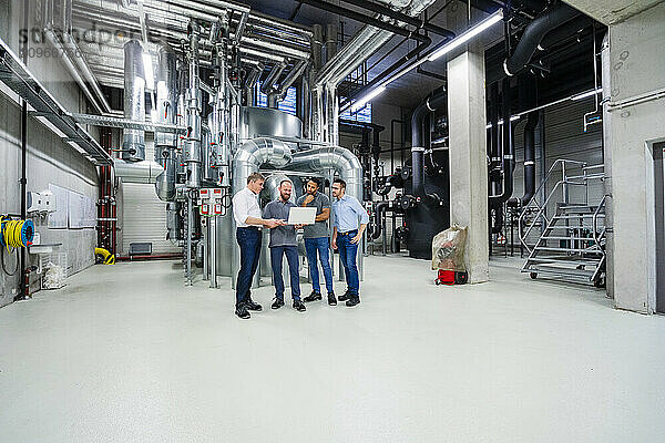 Businessmen and employees with laptop having a meeting in factory