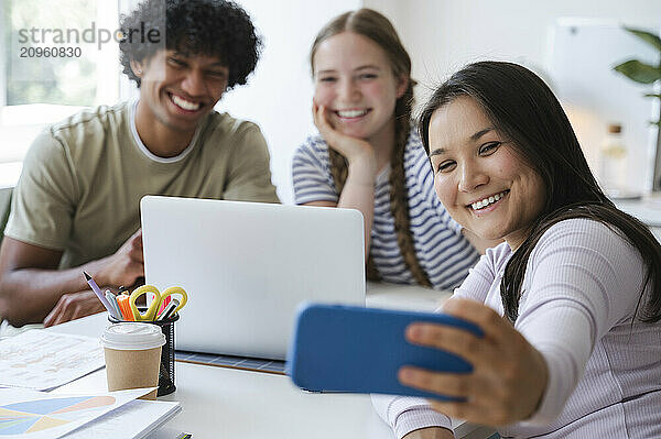 Smiling woman taking selfie through smart phone with friends at home