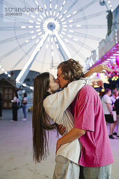 Romantic couple kissing against background of lights at amusement park