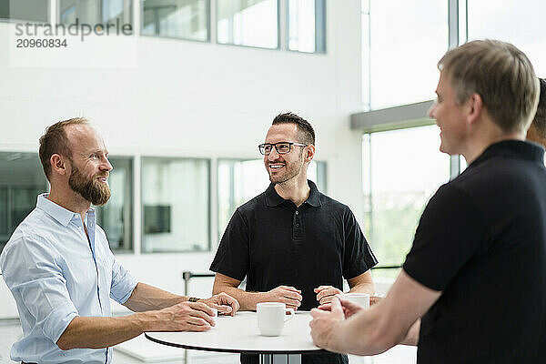 Group of businessman having informal meeting standing in office hall with cups of coffee