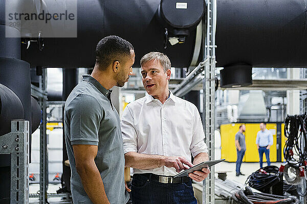 Employee and businessman with digital tablet talking in factory