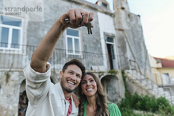 Happy woman with man holding keys standing in front of house