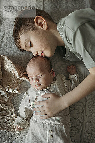 Cute boy with hand on baby brother lying on bed at home