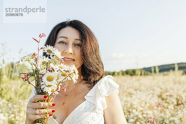 Beautiful mature woman holding bunch of daisy flowers in field