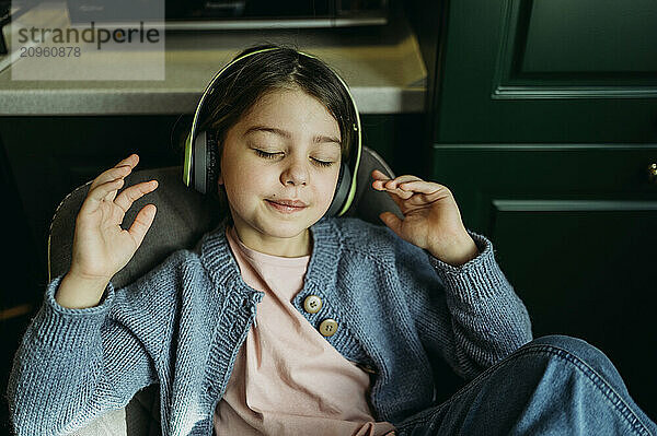 Carefree girl with eyes closed listening to music through wireless headphones at home