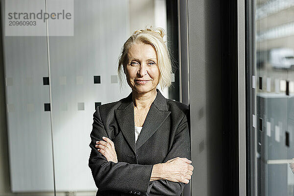 Confident businesswoman standing with arms crossed at office