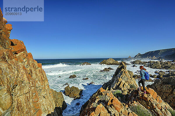 Traveler standing on rocks near Indian Ocean at Kranshoek Hiking Trail in Garden Route National Park  Western Cape  South Africa