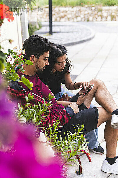 Man using smart phone with girlfriend sitting on bench