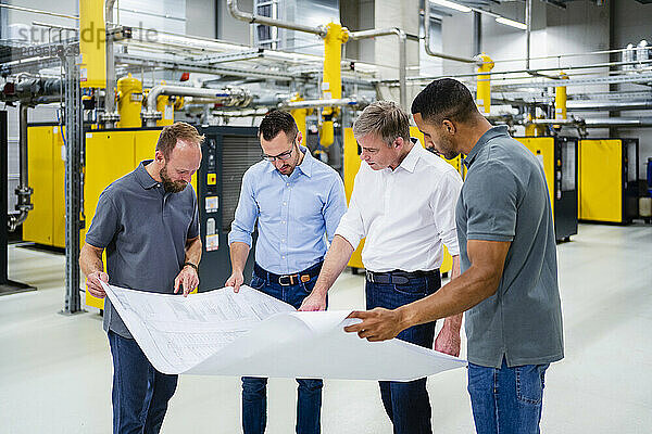 Businessmen and employees having a meeting in factory looking at plan