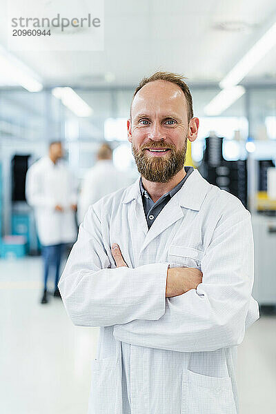 Confident electrical technician standing in electronics factory with arms crossed