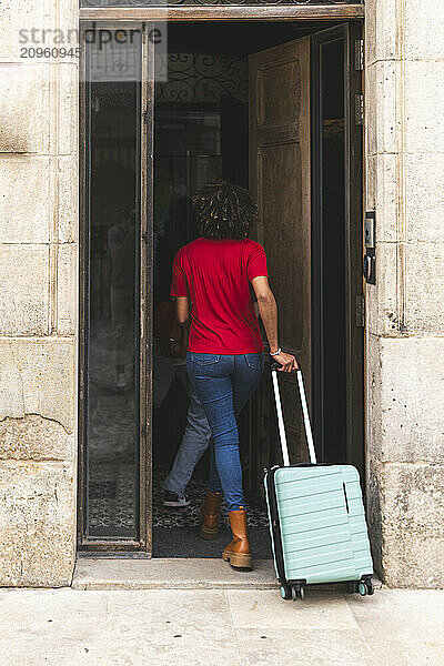 Woman holding luggage and entering through door in hotel