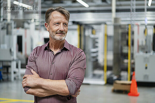 Thoughtful businessman with arms crossed at factory