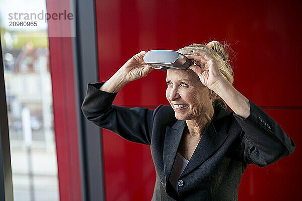 Excited senior businesswoman wearing virtual reality headset at office