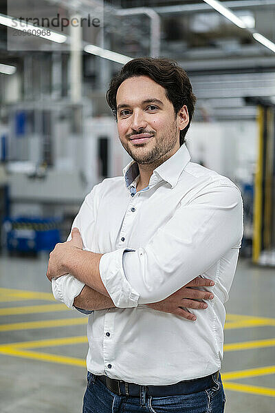 Confident businessman standing with arms crossed at factory