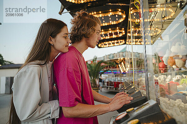 Couple playing toy grabbing game at amusement park