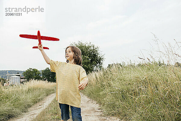 Boy playing with airplane toy standing on footpath near field