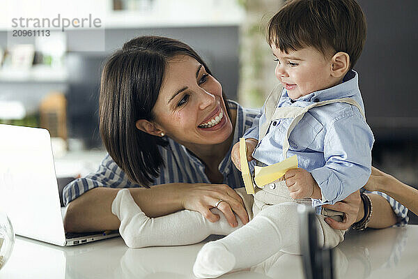 Baby boy holding sticky notes and playing with mother at home