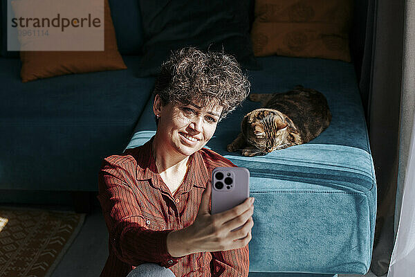 Smiling woman taking selfie with cat at home