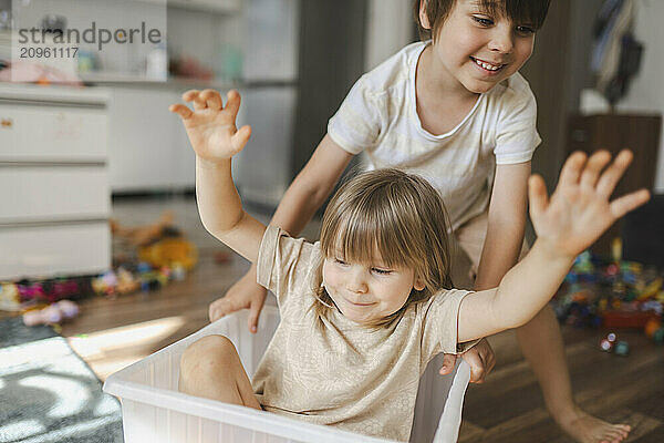 Happy girl sitting in plastic container and having fun with brother at home