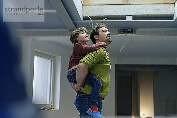 Father piggybacking son and standing in new apartment