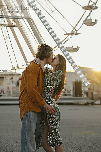 Happy couple kissing at sunset in amusement park