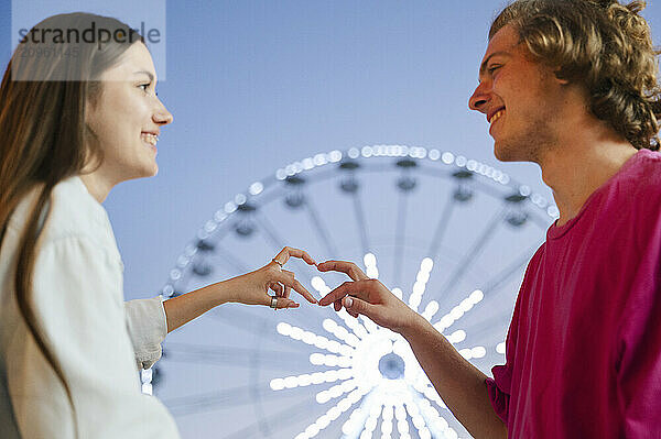 Smiling couple making heart symbol with hands at amusement park