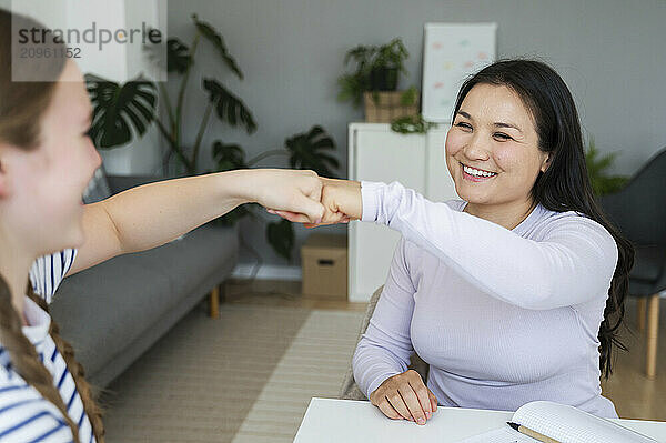 Smiling woman doing fist bump with friend at home