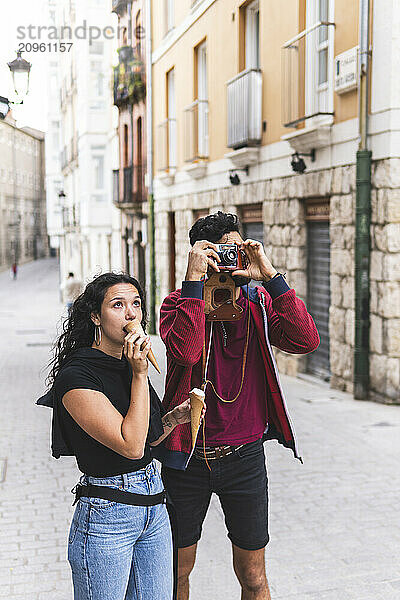 Man photographing through camera with girlfriend eating ice cream at street