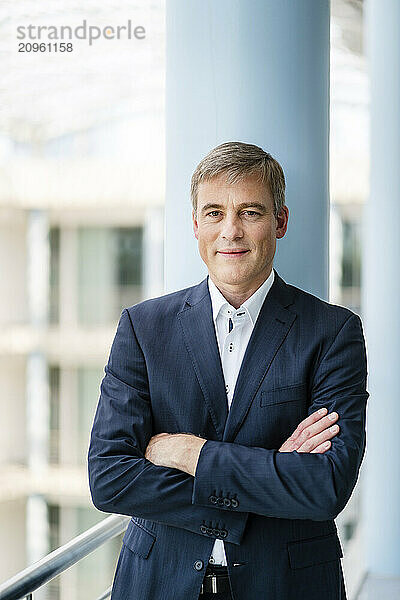 Successful businessman standing with arms crossed in front of column