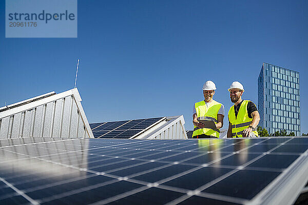 Two technicians utilizing a tablet PC while working on the rooftop of a commercial building equipped with solar panels