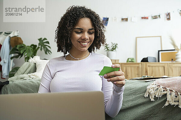 Happy teenage girl making payment through credit card at home