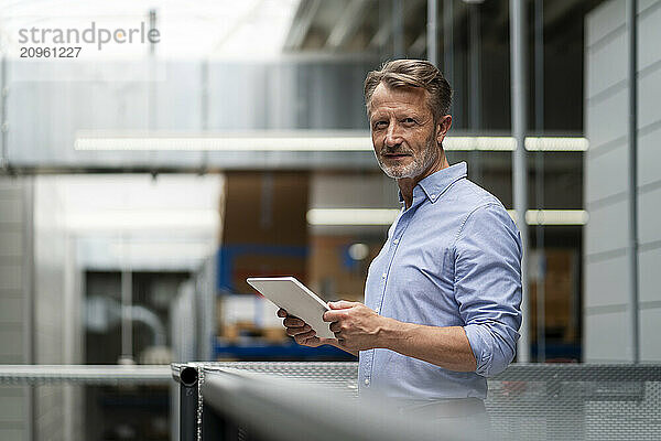 Senior businessman with tablet PC near railing in factory