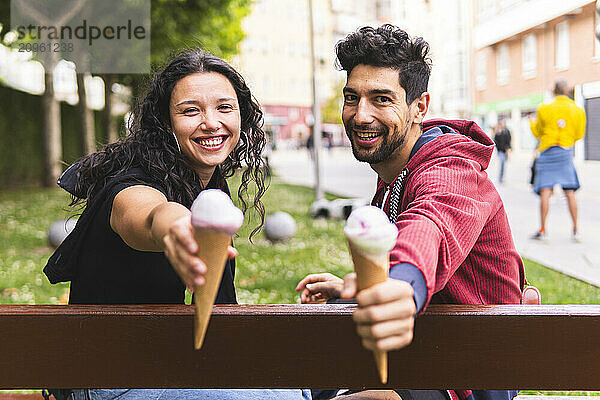 Happy couple showing ice cream and sitting on bench in city