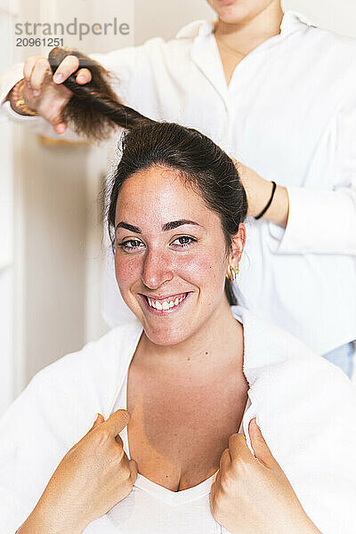 Smiling woman getting hair tied by friend at home