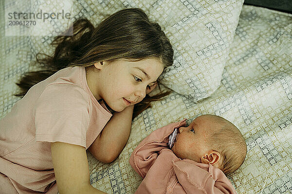 Newborn baby with pacifier lying near sister on bed