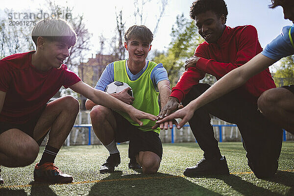 Smiling soccer players stacking hands on field